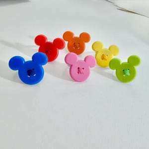 May include: Six colourful buttons in the shape of a mouse's head. The buttons are in blue, red, orange, pink, yellow, and green. Each button has contrasting thread sewn through the centre.