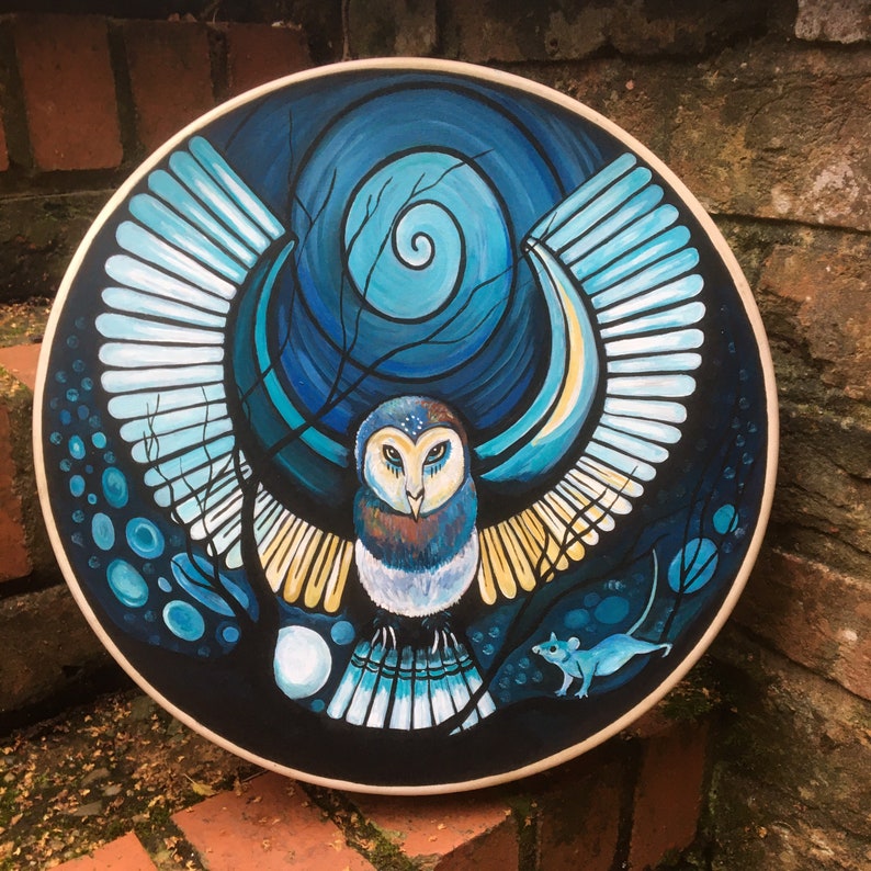 May include: Round wall art featuring a stylized owl with outstretched wings, painted in shades of blue, white, and yellow against a dark background. A small blue mouse is depicted at the bottom. The artwork is framed with a light-colored wooden border.