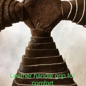May include: Close-up of a brown leather handle grip. The grip is made of layered strips of leather, forming a cone shape. The text "Leather handle grip for comfort" is visible in green.