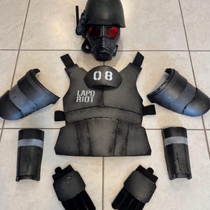 K&ouml;nnte beinhalten: Ein komplettes schwarzes taktisches Kost&uuml;mset, einschlie&szlig;lich eines Helms mit einer Gasmaske mit roten Linsen, einer Weste mit dem Aufdruck "LAPD RIOT" und "08", Arm- und Beinsch&uuml;tzern sowie Handschuhen. F&uuml;r Cosplay oder Themenveranstaltungen.