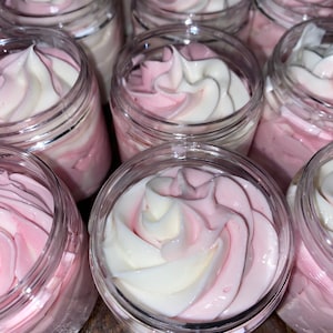 Op de afbeelding: Meerdere potten met roze en witte swirl whipped body butter. De potten zijn van helder glas met een wit deksel.
