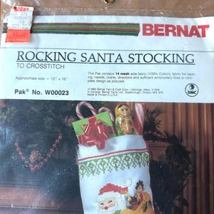 May include: A Bernat Rocking Santa Stocking cross-stitch kit in a clear plastic package. The label reads Rocking Santa Stocking to crosstitch, Pak No. W00023, and lists an approximate size of 12 inches by 16 inches. The kit includes 14 mesh aida fabric.