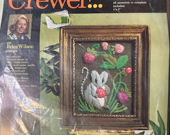 Puede incluir: Un paquete de kit de bordado Creative Crewel de Columbia-Minerva para un cuadro de ratón gris 7226. El empaque incluye texto, una foto de Erica Wilson y una imagen de un bordado enmarcado que muestra un ratón gris sosteniendo una fresa roja.