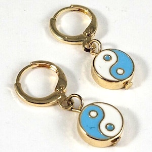May include: Gold hoop earrings with a dangling charm featuring a yin yang symbol with blue and white enamel.