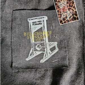 May include: Dark denim fabric with a pocket displaying a light grey guillotine graphic and the text "Billionaires Should Exist". A small card with a guillotine design on a leopard print background is also visible.