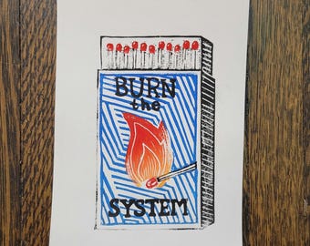May include: A blue and white matchbox with a red and orange flame illustration. The text "BURN the SYSTEM" is printed on the matchbox.