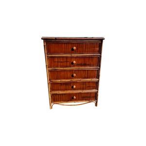 May include: A tall, five-drawer chest of drawers made of bamboo. The drawers are a dark brown color with round, light-colored wooden knobs. The bamboo has a natural, textured appearance, and the chest has a curved base.