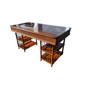 May include: A vintage desk with a glass top and a woven rattan frame. The desk has multiple shelves and a warm brown color. The design is reminiscent of mid-century modern furniture.