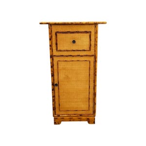 May include: A tall, narrow cabinet with a woven, light brown front and dark brown trim. The cabinet has a small drawer at the top with a round, black knob and a door below. The cabinet is made of bamboo.
