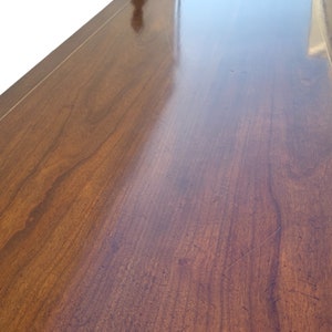 May include: Close-up of a smooth, dark wood surface with a light wood border. The surface is polished and reflects light.