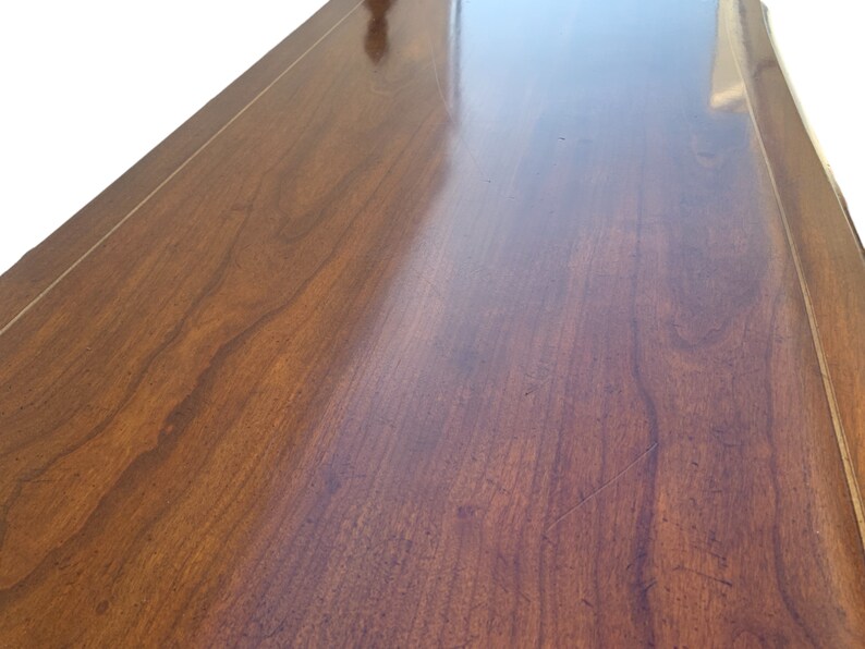 May include: Close-up of a smooth, dark wood surface with a light wood border. The surface is polished and reflects light.