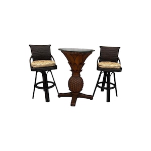 May include: A pub table with a dark brown wooden base carved in the shape of a pineapple and a round top, flanked by two dark brown woven wicker bar stools. Each stool features a square seat cushion with a light beige and brown leaf pattern.