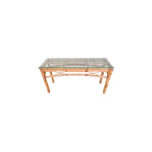 May include: Rectangular coffee table with a clear glass top and a light brown bamboo frame. The table has a curved design and is suitable for a living room or lounge area. The table measures approximately 48 inches long, 24 inches wide, and 18 inches high.