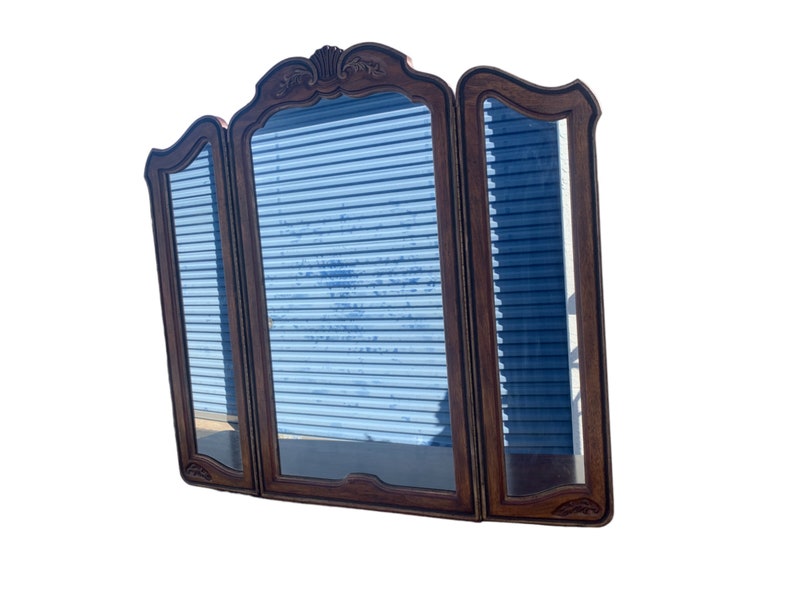 May include: A three-panel wooden mirror with a decorative carved frame. The mirror has a traditional style and is made of dark wood.
