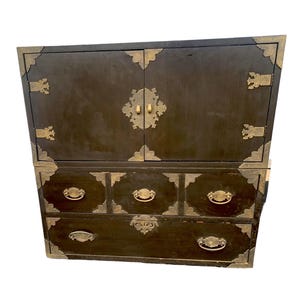 May include: A dark brown wooden cabinet with brass hardware and five drawers. The cabinet has two doors on the top and four drawers on the bottom.