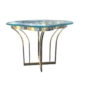 May include: A gold metal table with a clear glass top. The table has a unique, organic shape and a simple, modern design.