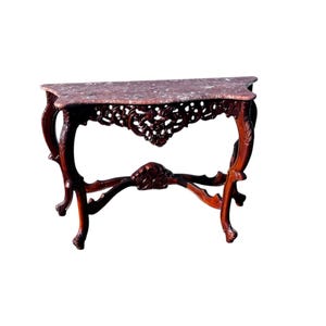May include: A dark wood console table with a marble top. The marble is a mottled pink color. The table has ornate carved details on the legs and apron. The table is approximately 30 inches long, 12 inches wide, and 30 inches tall.
