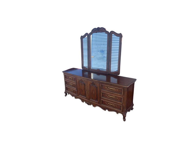 May include: A dark wood dresser with six drawers and a three-panel mirror. The dresser has ornate carvings and gold accents.