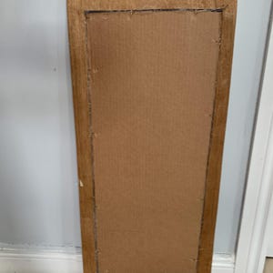 Op de afbeelding: Een rechthoekige houten spiegel met een gesneden ontwerp aan de bovenkant. De spiegel is rechthoekig en heeft een bruin houten frame.