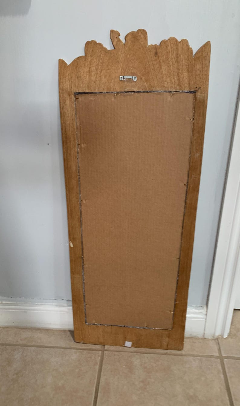 Op de afbeelding: Een rechthoekige houten spiegel met een gesneden ontwerp aan de bovenkant. De spiegel is rechthoekig en heeft een bruin houten frame.