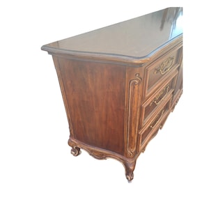 May include: A dark wood dresser with ornate carvings and gold-toned hardware. The dresser has six drawers and a curved top.