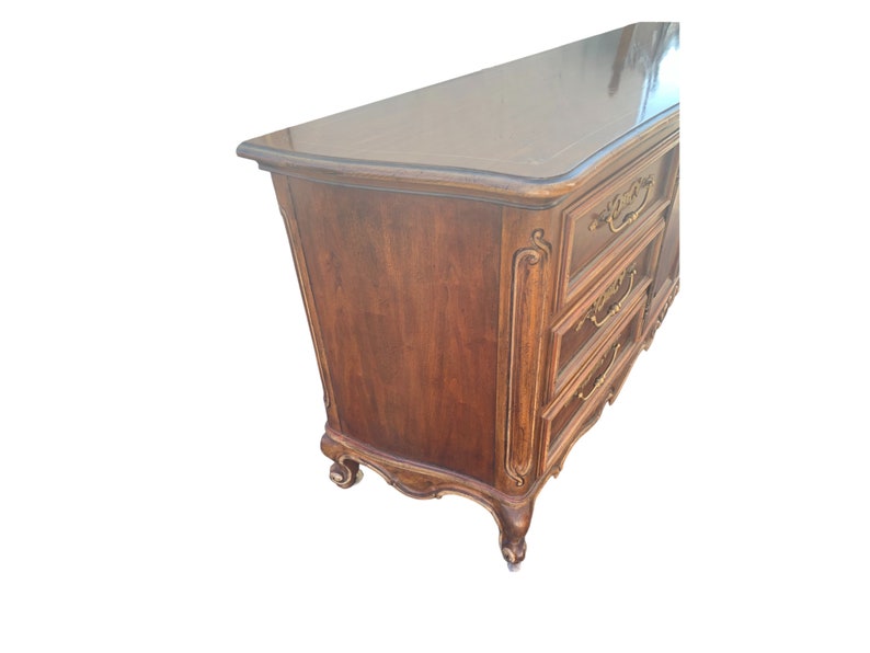 May include: A dark wood dresser with ornate carvings and gold-toned hardware. The dresser has six drawers and a curved top.