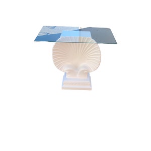 May include: White table with a glass top and a base shaped like a seashell.