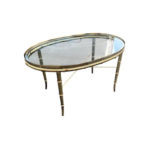 May include: Oval glass-top coffee table with a brass frame and faux bamboo legs.