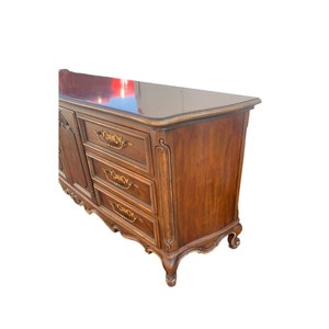 May include: A wooden dresser with six drawers and ornate gold-colored hardware. The dresser has a dark wood finish and a curved top.