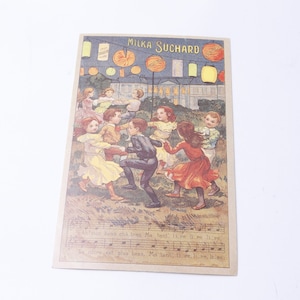 May include: Vintage postcard featuring a group of children dancing in a circle under a string of lanterns. The postcard is advertising Milka Suchard chocolate with the text "Milka Suchard" printed at the top. The postcard has a musical score at the bottom with the text "An'j'ean hond cha treng Ma tant, Il're il me si'c, Je t'aime, c'est plus beau, Ma tant, Il're il me si'c."