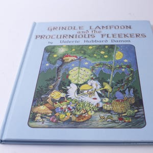 May include: A blue book with the title "Grindle Lamfoon and the Proclurnious Fleekers" by Valerie Hubbard Damon. The cover features an illustration of a whimsical scene with a bird playing a trumpet, surrounded by flowers and other creatures.