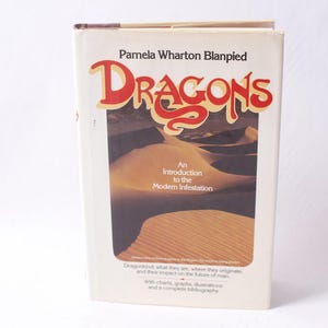 May include: A vintage book titled "Dragons" by Pamela Wharton Blanpied. The cover features the title in red and gold lettering, with an illustration of sand dunes. The book's subtitle reads "An Introduction to the Modern Infestation."