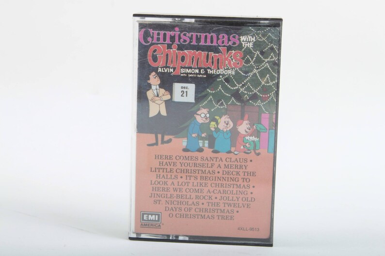 May include: A vintage cassette tape featuring the Alvin and the Chipmunks Christmas album. The cassette tape cover features a cartoon illustration of Alvin, Simon, and Theodore standing in front of a Christmas tree. The text on the cover reads "Christmas with the Chipmunks Alvin Simon & Theodore" and includes a list of songs on the album.
