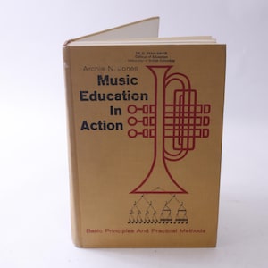 May include: A gold book with a red trumpet illustration on the cover. The title is "Music Education in Action: Basic Principles and Practical Methods" by Archie N. Jones.
