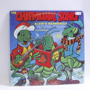 May include: A vintage vinyl record album cover featuring three cartoon grasshoppers dressed in winter clothing. The album is titled "The Chipmunk Song - Alvin's Harmonica" and features the text "The Christmas Songs" on the cover.