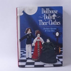 May include: Book cover featuring the title "Dollhouse Dolls & Their Clothes" by Barbara Marston & Tina Bliss. The cover shows three dolls dressed in different outfits on a checkered floor.