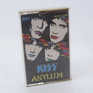 May include: A cassette tape with a black background and a colorful image of the band KISS. The text "KISS" and "ASYLUM" is printed in white on the tape.