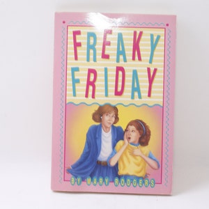 May include: A pink book with a yellow and blue title "FREAKY FRIDAY" by Mary Rodgers. The cover features an illustration of two women, one with brown hair and a blue jacket, the other with brown hair and a yellow shirt.