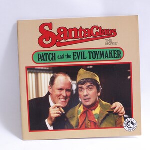 Puede incluir: Una portada de libro con una foto de dos hombres. El libro se titula "Santa Claus The Movie: Patch and the Evil Toymaker".