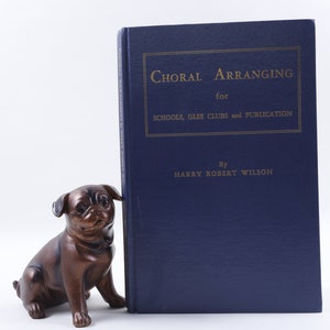 Könnte beinhalten: Ein blaues Hardcover-Buch mit dem Titel "Choral Arranging for Schools, Glee Clubs and Publication" von Harry Robert Wilson.