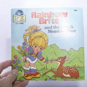 May include: A vintage Rainbow Brite book and record set featuring a colorful illustration of Rainbow Brite with a deer. The book is titled "Rainbow Brite and the Meadow Deer".