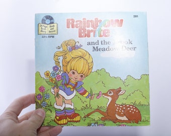 Può includere: Un set vintage di libro e disco di Rainbow Brite con un'illustrazione colorata di Rainbow Brite con un cervo. Il libro è intitolato "Rainbow Brite e il cervo del prato".