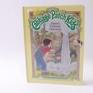 Puede incluir: Un libro infantil vintage titulado "Cabbage Patch Kids: Xavier's Fantastic Discovery". La portada presenta una ilustración de un niño con overoles, una cascada y personajes de dibujos animados. El libro tiene una cubierta amarilla.