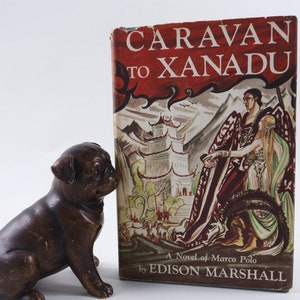 May include: A vintage hardcover book titled "Caravan to Xanadu" by Edison Marshall. The cover features a colorful illustration of a man and woman in a fantastical setting.