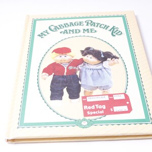 Può includere: Un libro intitolato "My Cabbage Patch Kid and Me" con una copertina verde e gialla. La copertina presenta due bambole Cabbage Patch Kids, una con i capelli biondi e una camicia rossa e l'altra con i capelli castani e un vestito blu. Il libro ha anche un'etichetta rossa che dice "Red Tag Special".