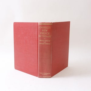 May include: A red hardback book titled "Cassell's New French Dictionary" with gold lettering. The book is open and the spine is visible. The book is published by Funk & Wagnalls Company.