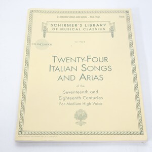 Puede incluir: Una cubierta de libro amarilla con un borde verde. El título es "Twenty-Four Italian Songs and Arias" de los siglos XVII y XVIII. El libro es para voz media alta.