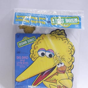 May include: A vintage Sesame Street "Big Bird and Little Bird's Dig and Little Book" in a clear plastic package. The book features a yellow Big Bird character and a smaller orange bird. The package includes the text "Sesame Street" and "Featuring Jim Henson's Muppets."