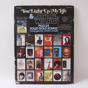 Puede incluir: Una portada de libro en blanco y negro con el título "You Light Up My Life & Star Wars" y una lista de 24 canciones de oro sólido arregladas por John Clausi.