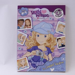 May include: A purple and pink book cover with a cartoon girl holding a camera. The book title is "Holly Hobbie & Friends: The Greatest Vacation" and the book is part of the "Simon Scribbles" series.